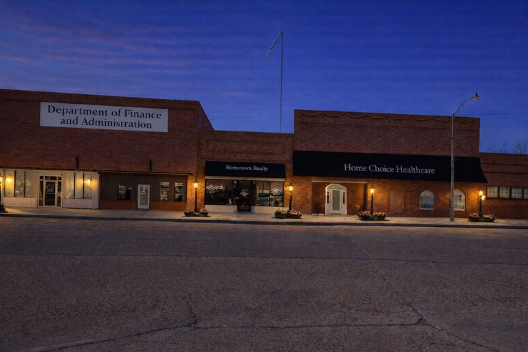 Department of Finance and Administration, Hometown Realty, and Home Choice Healthcare evening storefront showcasing downtown businesses and services